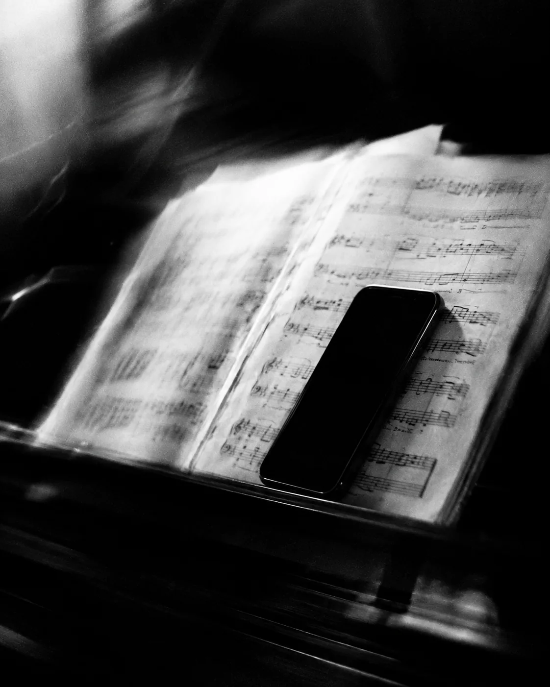 A black phone resting on an open book of sheet music in soft, grainy light.